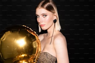 Young gorgeous and elegant woman with golden color balloon celebrating birthday or other occasion while standing in front of camera