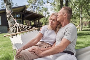 Freudiger liebender Mann und Frau entspannen sich in der Hängematte während der Freizeit im Hof des Ferienhauses