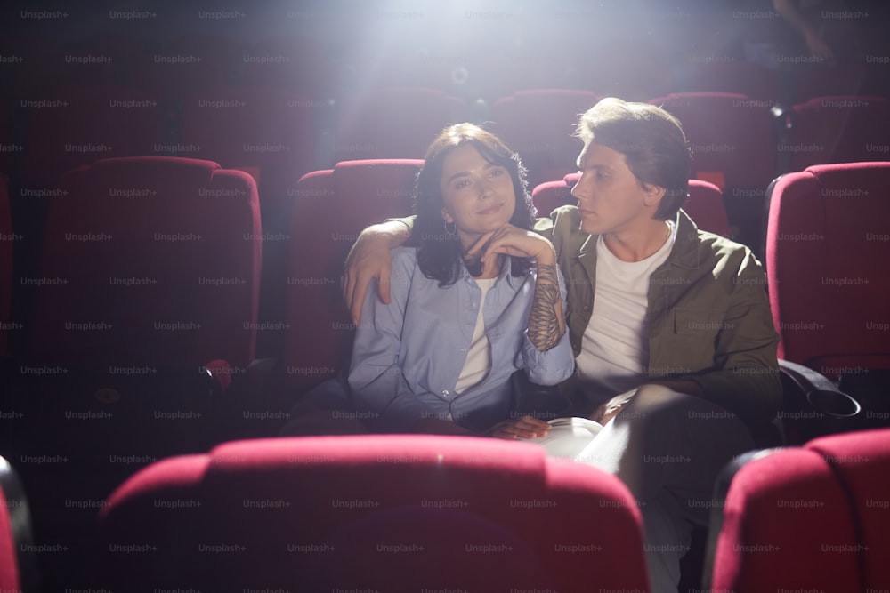 Retrato de una joven pareja amorosa en el cine viendo una película mientras disfruta de una cita, un hombre mirando a su novia con afecto y abrazándola, copiando el espacio