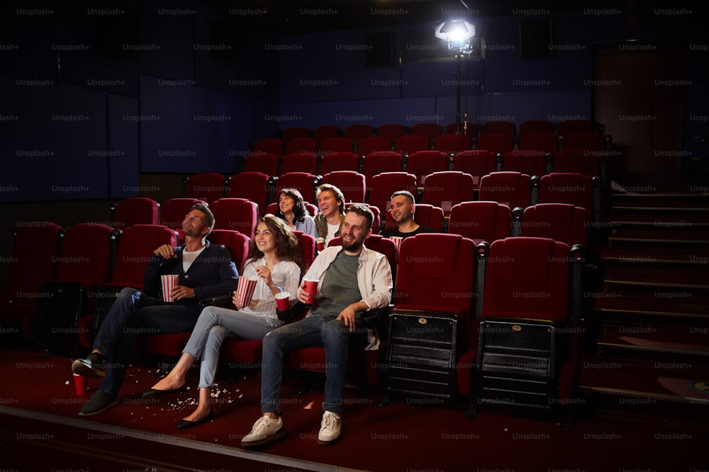 Wide angle view at group of friends watching movie in cinema while enjoying private viewing in empty hall, copy space