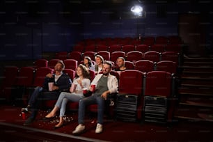 Wide angle view at group of friends watching movie in cinema while enjoying private viewing in empty hall, copy space