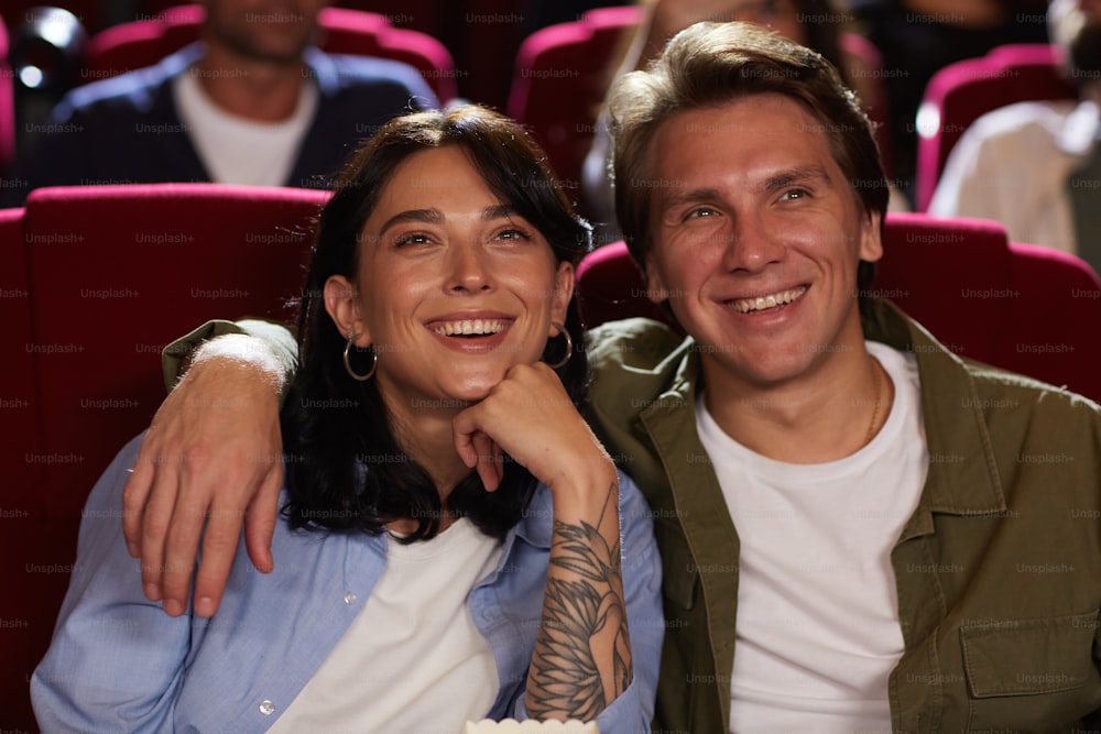 Ritratto della vista frontale della giovane coppia sorridente al cinema che guarda il film e abbraccia mentre si gode l'appuntamento romantico