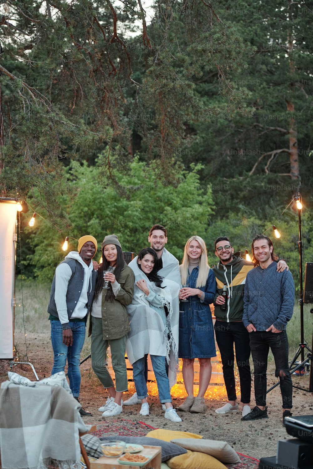 Several affectionate young restful friends standing in front of camera on background of lights and green trees in natural environment