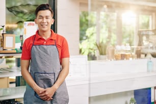 Retrato del sonriente joven vietnamita propietario de un coffeeshop parado en el mostrador