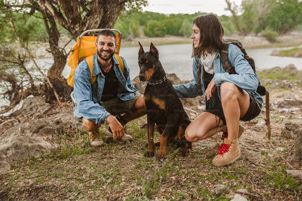 트레킹 등산객 커플과 그들의 개는 배낭과 함께 트레일 트레킹에서 비를 맞으며 걷고, 건강하고 활동적인 라이프 스타일을 제공합니다.