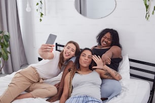 白人とアフリカ系アメリカ人の女性の親友が、楽しい自撮りのポーズをとりながら変な顔をする