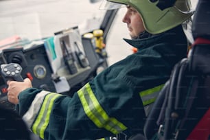 Side view portrait of seriously male wearing green protective uniform and helmet on head while controlling process of team work