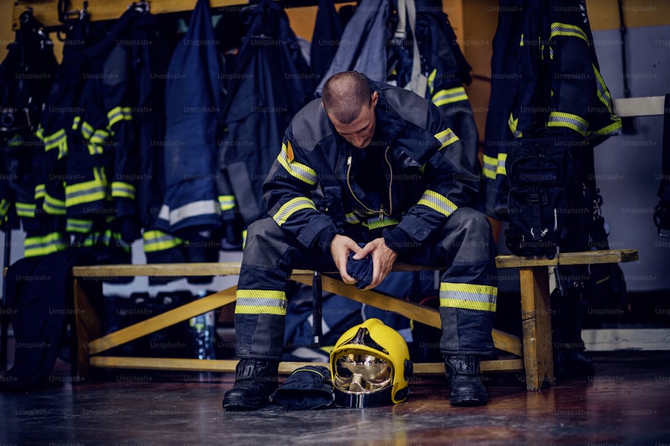 Young attractive fireman in protective uniform sitting in fire station ...