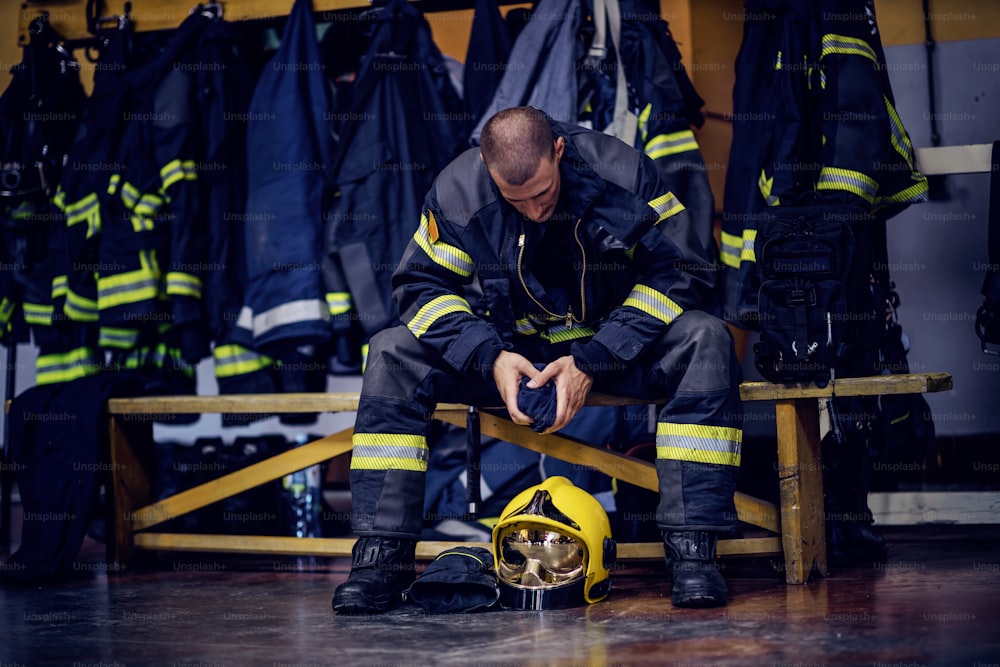 Young attractive fireman in protective uniform sitting in fire station and waiting for other firemen. He is prepared for action.