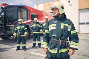 Waist up portrait of man at the workplace while looking away with firefighter crew in behind of him