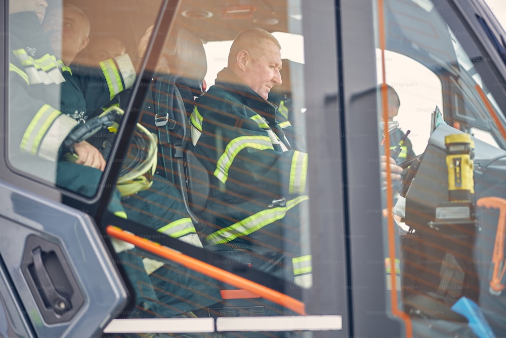 Adult men wearing green protective uniform with equipment heading to emergency place in fire truck