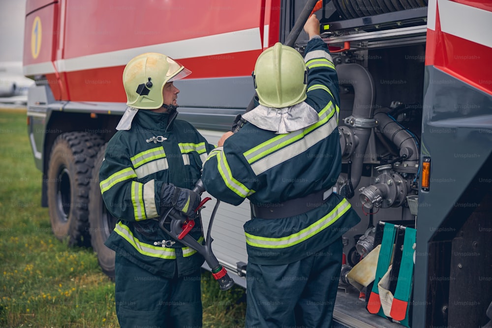 Retrato de dos bomberos con cascos amarillos usando equipos para situaciones de emergencia