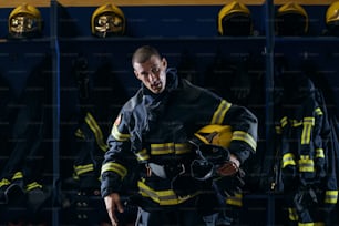 消防署に立っている間、行動後に脇の下にヘルメットを持つ保護制服を着た勇敢な若い魅力的な消防士。