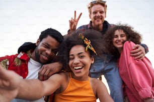 Portrait of four merry young people spending warm evening outdoors and taking selfie with sky on background