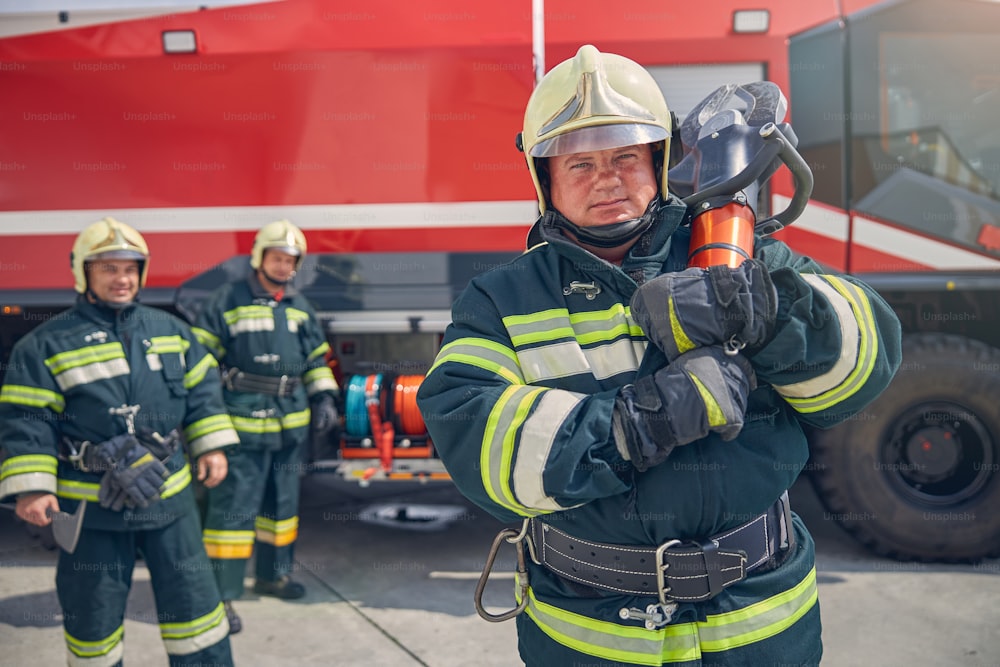 Reifer, starker Feuerwehrmann, der mit Ausrüstung in der Hand an der Fotokamera posiert