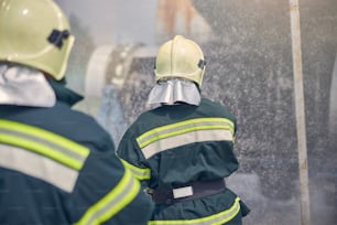 Rückansicht der Feuerwehr mit kompletter Ausrüstung und sicheren Helmen auf dem Kopf, die Wasser aus dem Schlauch spritzen