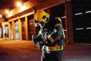 Vigile del fuoco in uniforme protettiva con equipaggiamento completo che si prepara a prendersi cura di grandi incendi.