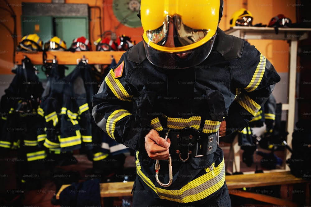 Fireman putting on protective uniform and preparing for action while standing in fire station.