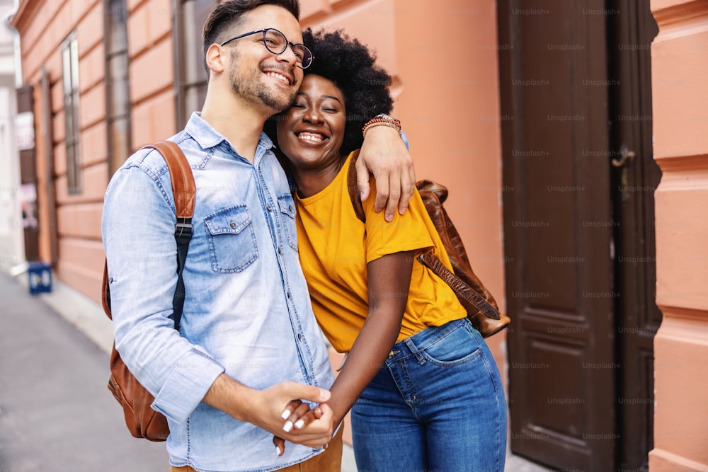 Young attractive multicultural couple hugging and walking on the street.