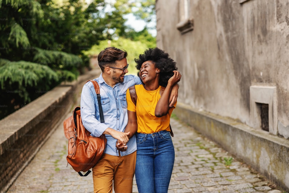 Young smiling cute multicultural hipster couple walking in an old town, hugging and flirting.