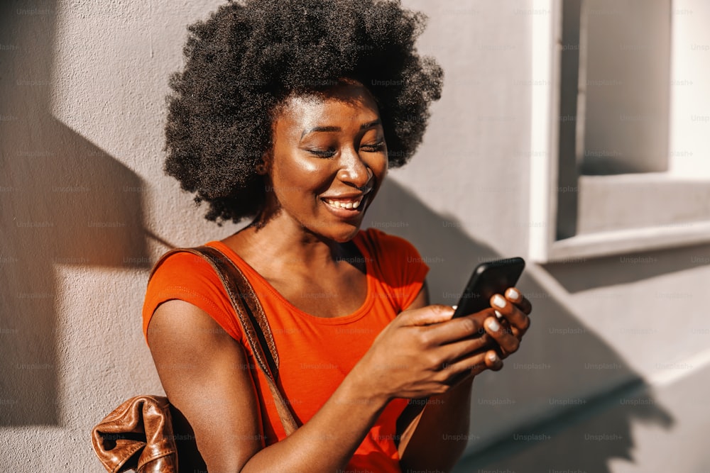 Young attractive african woman standing outdoors and using smart phone.