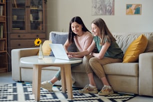 Adolescente riendo y su feliz madre sentada en el sofá frente a la computadora portátil mientras discuten y eligen productos en la tienda en línea