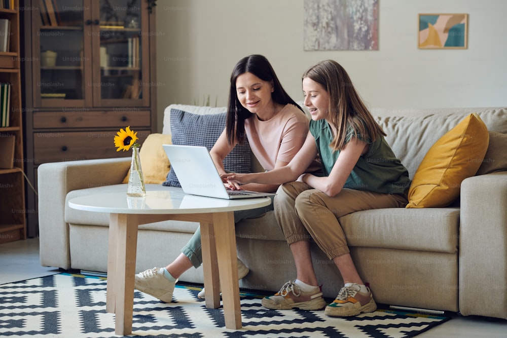 Adolescente rindo e sua mãe feliz sentada no sofá em frente ao laptop enquanto discute e escolhe produtos na loja on-line