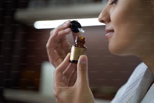 Primer plano de una mujer feliz oliendo aceite hidratante para la piel mientras está de pie en el salón de belleza