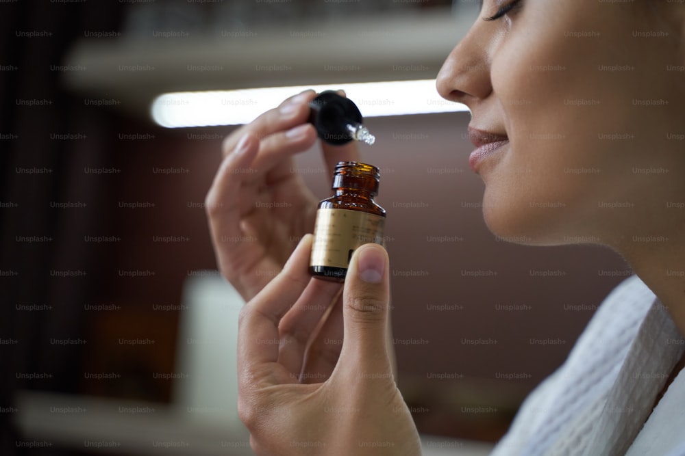 Close up of happy lady smelling moisturizing oil for skin while standing in beauty salon