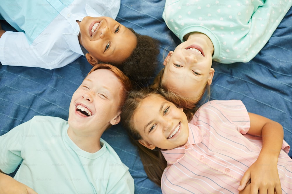 Top view close up of multi-ethnic group of kids lying in circle on blanket outdoors and looking at camera