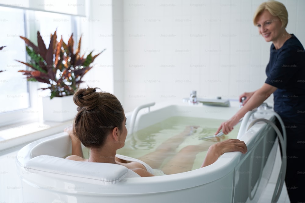 Mulher relaxada recebendo hidromassagem de esteticista profissional no centro de spa