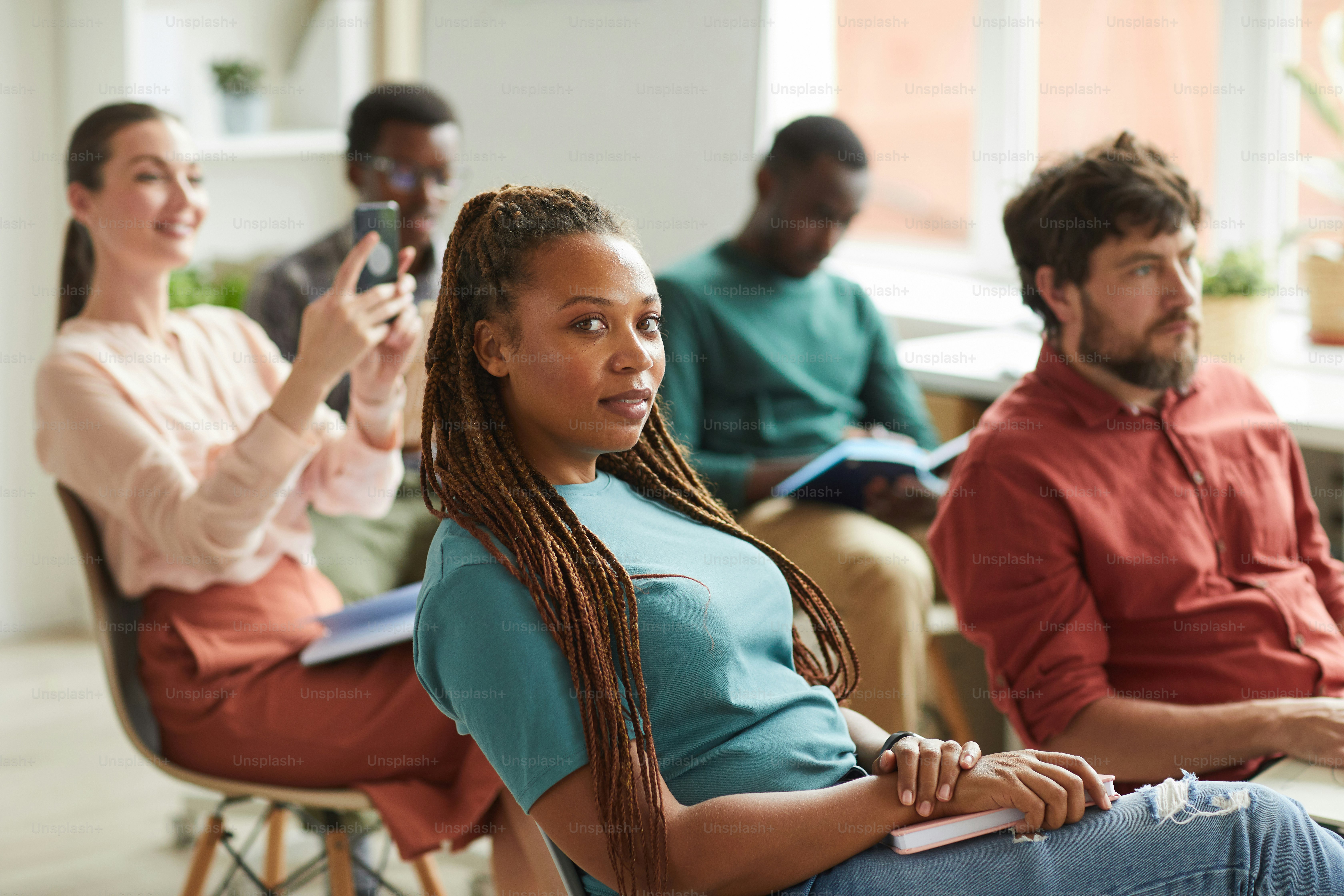 Grupo multiétnico de pessoas sentadas na plateia durante seminário de treinamento ou conferência de negócios no escritório, foco na mulher afro-americana olhando para a câmera em primeiro plano, espaço de cópia