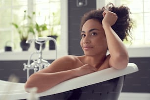 Smiling young female is relaxing and thinking over new day while having bath at home