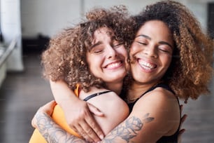 Waist up of smiling pretty female friends hugging while closing their eyes and dreaming