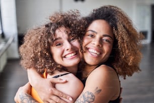 Waist up of happy pretty ladies hugging while looking at camera in studio