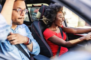 Joven y atractiva pareja multicultural hipster sentada en coche y conduciendo.
