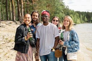 Portrait of cheerful young interracial friends standing with beer bottles on beach