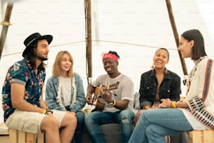 Jóvenes amigos interraciales positivos sentados en una tienda de campaña y escuchando música interpretada por guitarrista negro