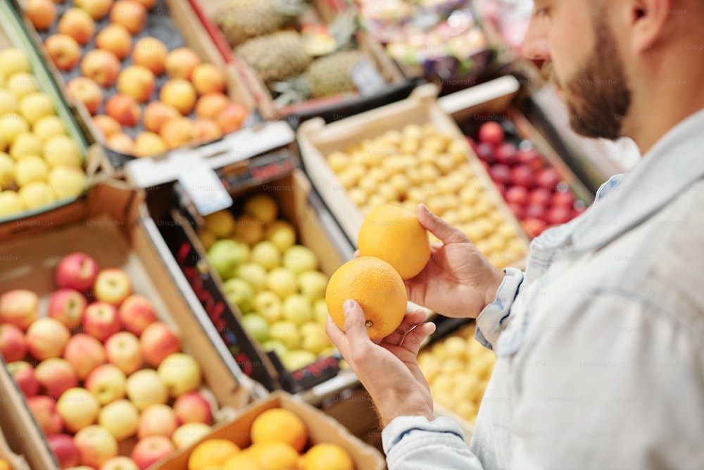 Vista sobre o ombro do homem barbudo em pé no balcão de comida e comprando frutas cítricas para fortalecer a imunidade no mercado