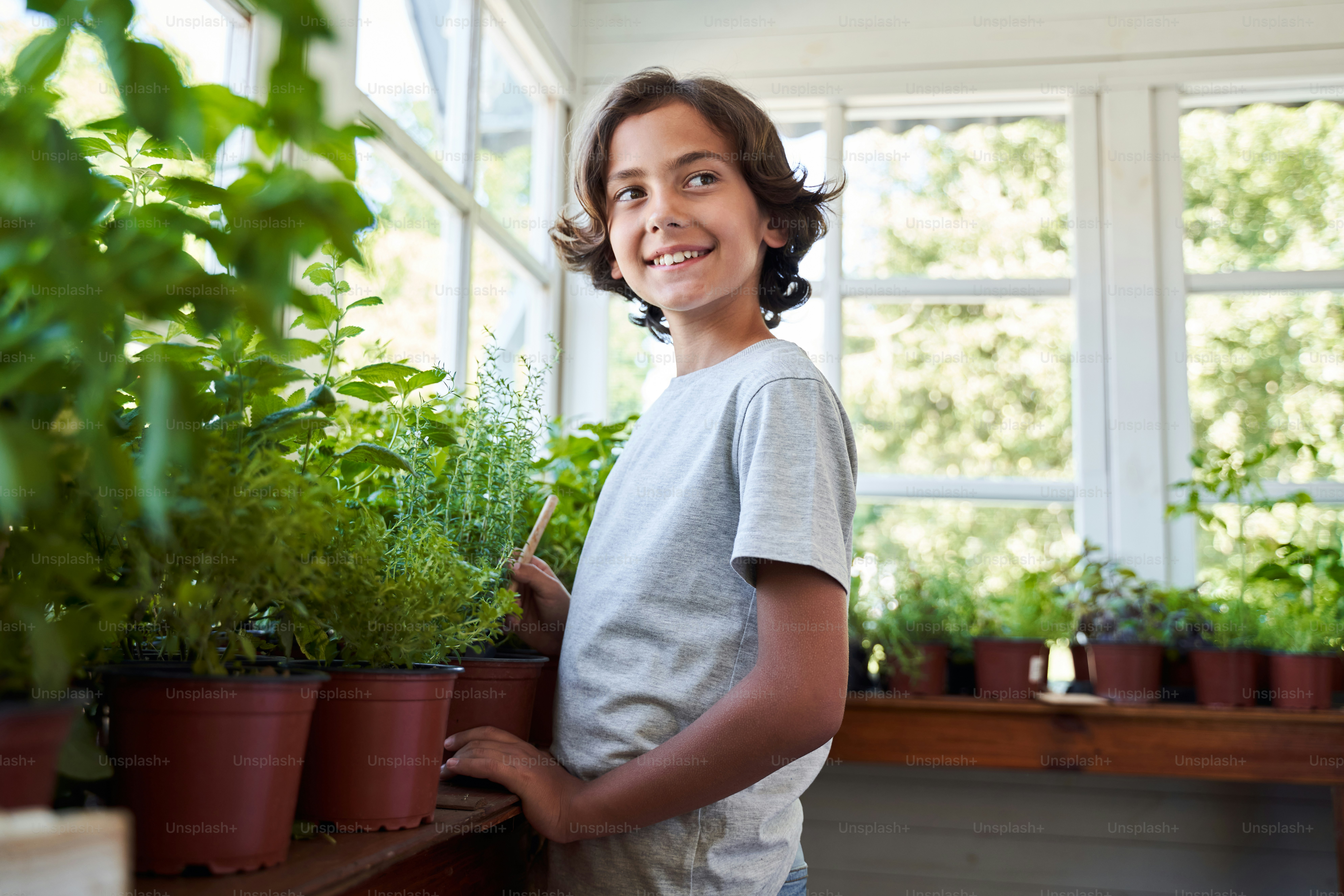 Joyful boy using gardening instrument and smiling while looking after houseplants at home