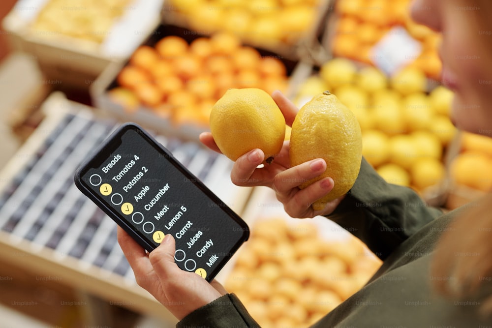 슈퍼마켓에서 레몬을 사는 동안 스마트폰으로 체크리스트를 사용하는 여성의 클로즈업