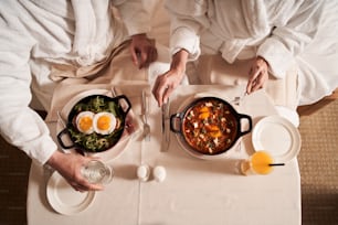 목욕 가운을 입은 커플이 달걀 식사와 건강 음료와 함께 테이블에 앉아 있습니다. 음식이 있는 테이블의 평면도