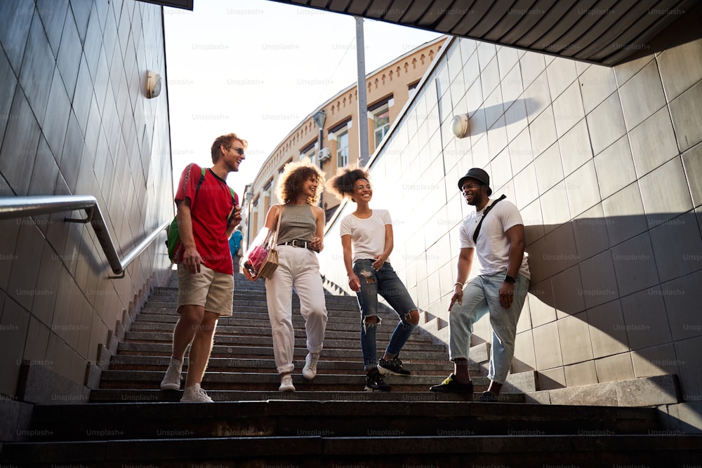 Ángulo bajo de cuatro amigos alegres bajando las escaleras en el metro mientras se divierten en el centro de la ciudad