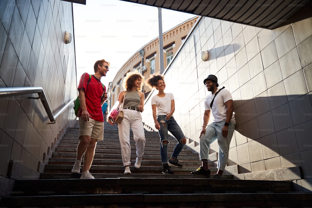 Niedriger Winkel von lustigen vier Freunden, die die Treppe hinunter in die U-Bahn gehen, während sie Spaß im Stadtzentrum haben