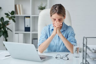 Contemporary businesswoman keeping her hands by face while brainstorming or trying to concentrate on work in office