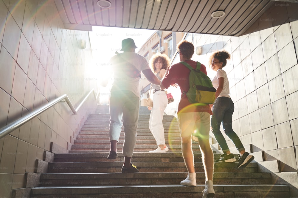 Low angle of four smiling friends going upstairs and having fun together while leaving underground