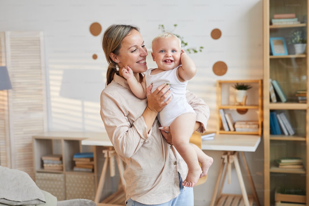 Horizontal medium shot of happy young woman holding her cute baby son in arms, copy space