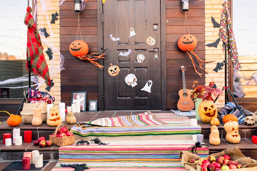 Door of country house decorated with halloween symbols in front of staircase with jack-o-lanterns, spiders, bats, apples and candles