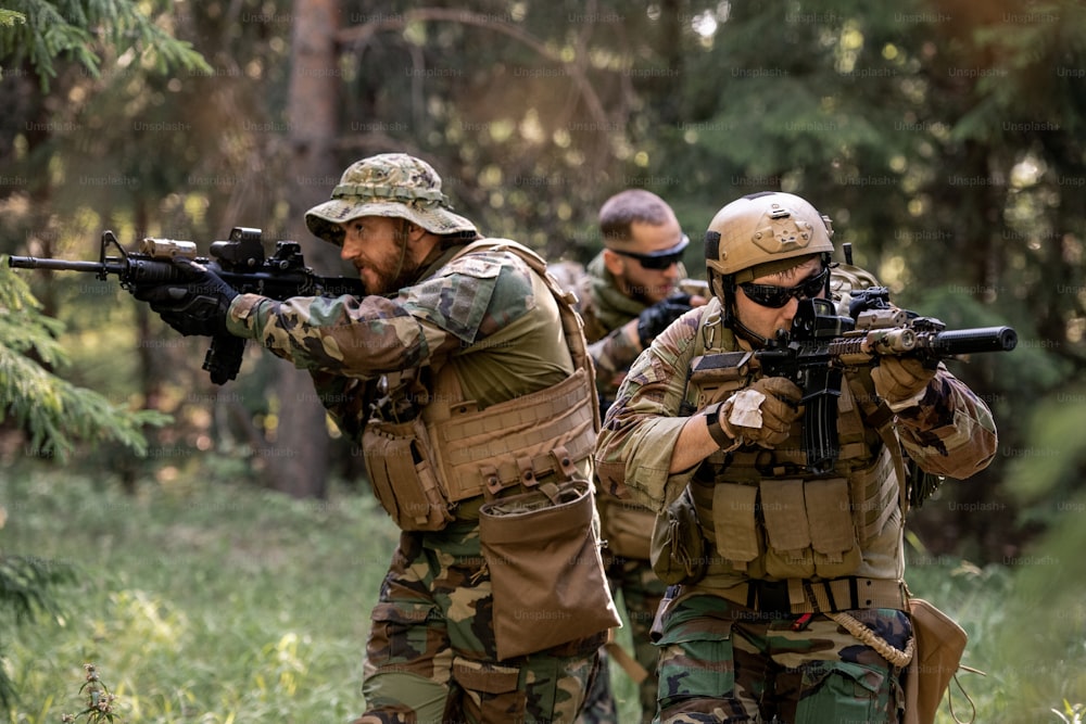 Grupo de soldados armados atentos en trajes de camuflaje moviéndose con rifles en el bosque mientras trabajan en la operación de limpieza