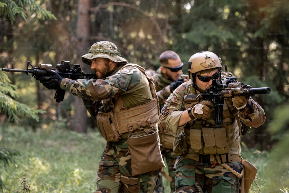 Group of attentive armed soldiers in camouflage outfits moving with rifles in forest while working at clean-up operation